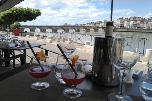 three wine glasses sitting on a table with a view of a bridge at Escapade Mâconnaise Spa-Sauna-Ciel de pluie tropicale-Champagne Nuit Romantique in Mâcon