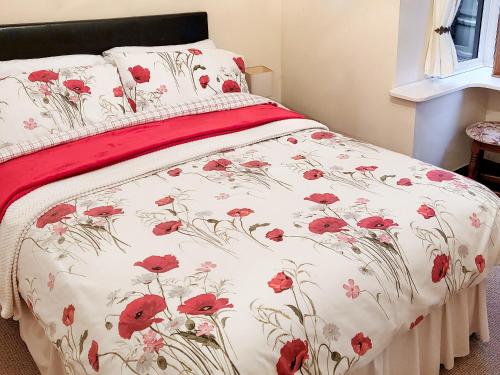 a bed with a red and white bedspread with red flowers at Elm Barn View in Freethorpe