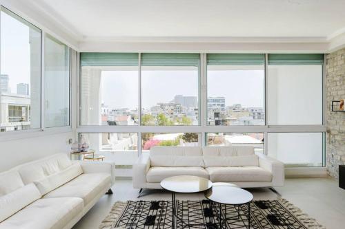 una sala de estar con muebles blancos y ventanas grandes. en Into the Jacuzzi by HolyGuest, en Tel Aviv
