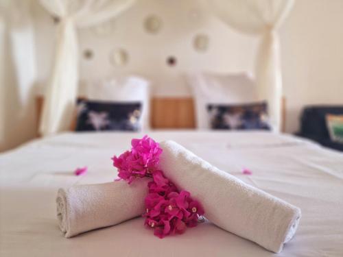 a rolled up towel with pink flowers on a bed at Hotel Le Manguier in Quartier Morne Pavillon