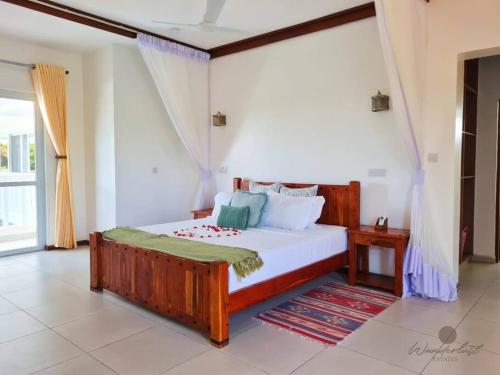 um quarto com uma grande cama de madeira e uma janela em Fiorella Beach House, Diani Beach em Praia de Diani