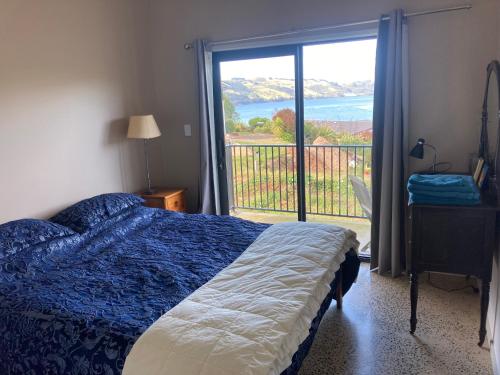 a bedroom with a bed and a balcony with a view at Commanding Harbour views exquisite sunset vista in Dunedin