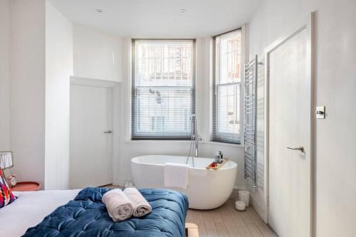 a white bathroom with a tub and a bed and a sink at Chelsea Posh apartment in London