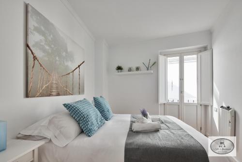 a white bedroom with a large bed with blue pillows at Dulce Arbolí Little Apartments in Cádiz