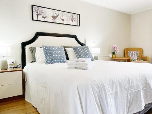 a bedroom with a bed with white sheets and blue pillows at Pupuke Manor Motel in Auckland