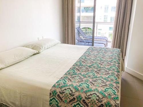 Bett mit einer Decke in einem Zimmer mit Fenster in der Unterkunft Apartamento de 2 quartos no luxuoso condomínio Jay in Florianópolis