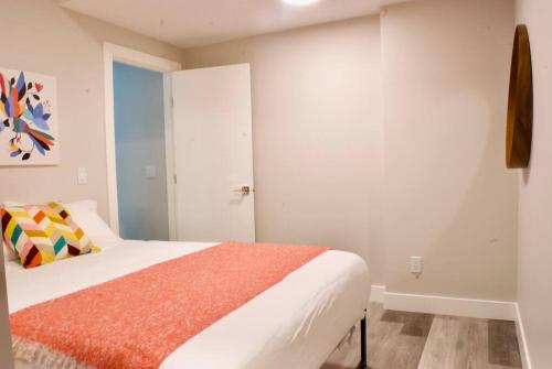 ein weißes Schlafzimmer mit einem Bett mit einer orangefarbenen Decke in der Unterkunft Modern 1br Home Full Kitchen Smarttv in Calgary