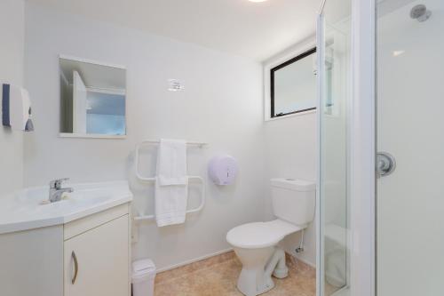 a white bathroom with a toilet and a shower at Kaiteriteri Reserve Cabins in Kaiteriteri