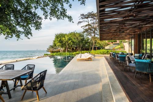 eine Außenterrasse mit Tischen und Stühlen am Wasser in der Unterkunft Andaz Pattaya Jomtien Beach, a Concept by Hyatt in Na Jomtien
