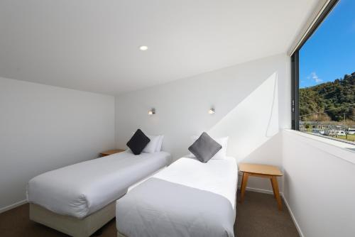 two beds in a room with a large window at Kaiteriteri Reserve Apartments in Kaiteriteri