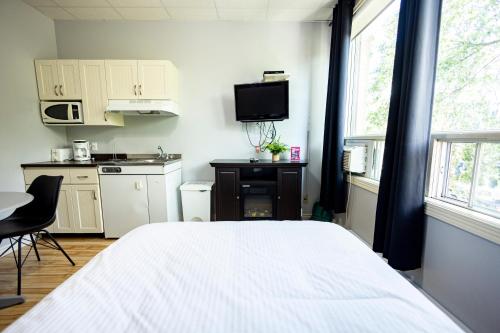 a bedroom with a white bed and a kitchen at Le Citadin in Rouyn