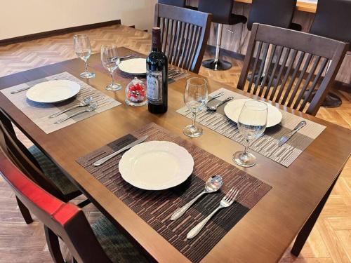a wooden table with plates and wine glasses on it at 団体歓迎ジョイサウンドカラオケ付き北軽井沢超大型貸別荘7寝室5浴室20人泊まれる in Karuizawa