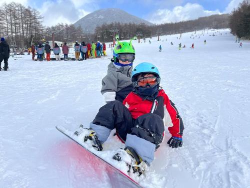 two children are sitting in the snow on a snowboard at 団体歓迎ジョイサウンドカラオケ付き北軽井沢超大型貸別荘7寝室5浴室20人泊まれる in Karuizawa