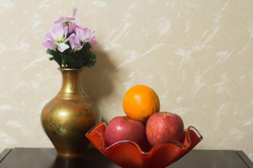 a bowl of apples and an orange and a vase with flowers at Mochida's Guest House in Tokyo