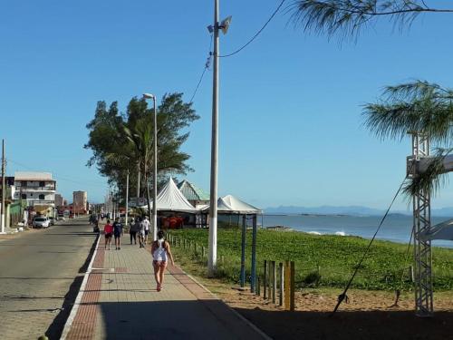 Una chica caminando por una acera junto a la playa en HOSPEDAGEM DA ROSE 3 en Marataizes