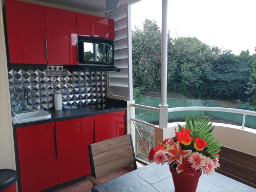 a kitchen with red cabinets and a table with a vase of flowers at STUDIO ROUGE GORGE TARTANE in La Trinité
