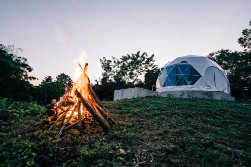 a tent and a fire in the grass next to a campfire at Family Getaway Dome Glamping w/ Private Hotspring in Lubo