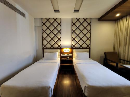 two beds in a room with a table and a chair at Hotel Preethi International in Mysore