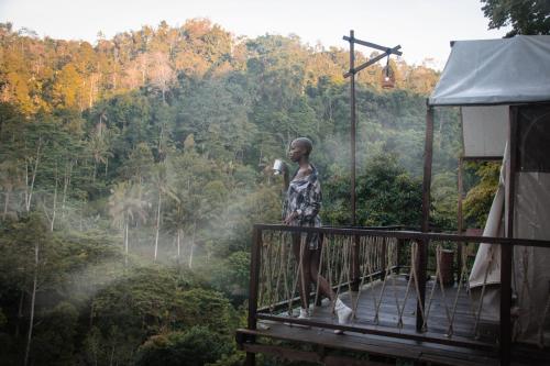 a woman standing on a balcony looking out at the forest at Glamping tent in Pelaga Eco Park in Patjung