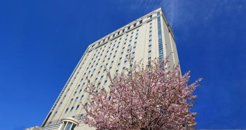 Hotel Lifort Sapporo في سابورو: مبنى طويل به شجرة مزهرة أمامه