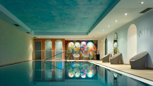 a swimming pool in a building with a painting on the wall at Hotel Der Heinrichshof in Lagundo