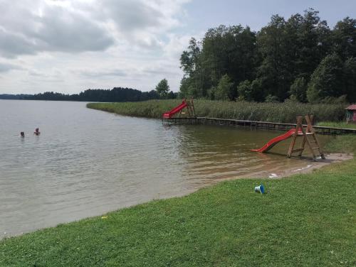 two people swimming in a river with a red slide at Ostoja Becejły in Szypliszki