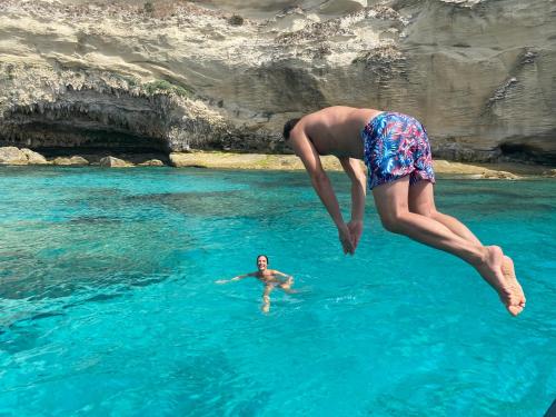two people jumping into the water in the ocean at Hotel Villa Del Parco in La Maddalena