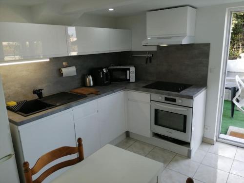 une cuisine avec des armoires blanches et un four à plaques de cuisson dans l'établissement Appartement Aurore en rez de jardin avec parking gratuit, à Vence