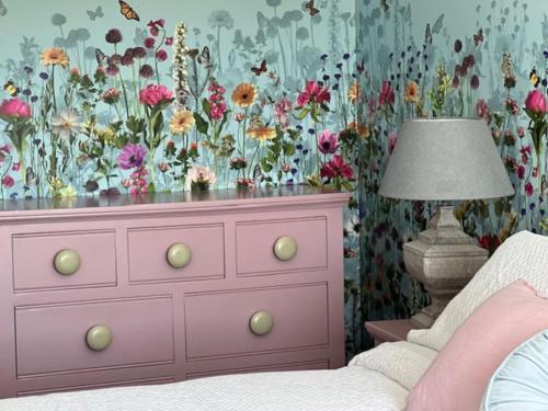 a bedroom with a pink dresser with a floral wallpaper at Cosy country cottage in rural location in Moffat