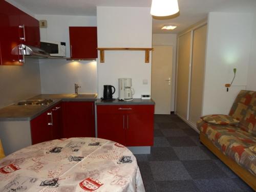 - une petite cuisine avec des placards rouges et un canapé dans la chambre dans l'établissement Studio cabine 4 pers, ski aux pieds, Les Menuires, 24m², balcon sud-ouest, proche commerces et remontées. - FR-1-178-101, aux Menuires