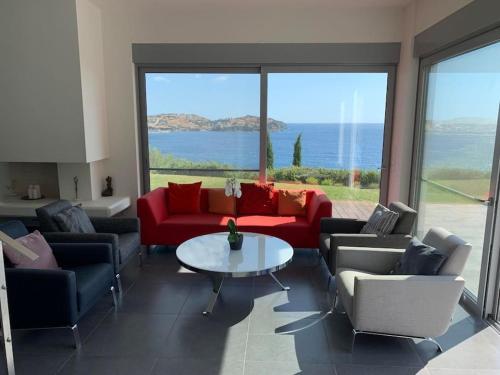 a living room with couches and a table and a large window at Villa Nafsika stunning view on the Aegean Sea in Áyioi Apóstoloi