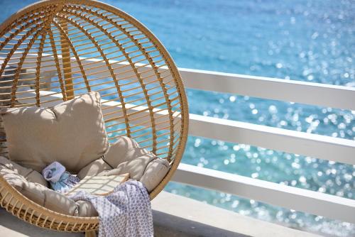 a rattan chair sitting on a balcony with the ocean at Anax Resort and Spa in Agios Ioannis Mykonos