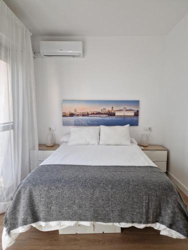 1 dormitorio con 1 cama blanca y una pintura en la pared en Floridos Playa Piso reformado de 2 habitaciones a 50m de la playa en Cala del Moral