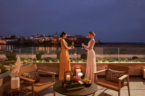 two women in dresses standing on a balcony at night at Fairmont La Marina Rabat Sale Hotel in Rabat