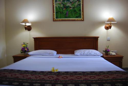 a bed in a bedroom with two lamps on the wall at Stana Puri Gopa Hotel in Sanur