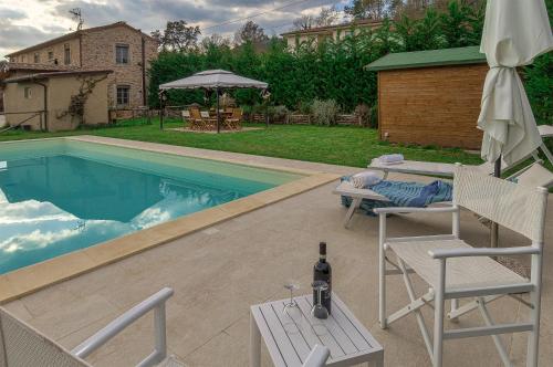 einen Pool mit 2 Stühlen, einem Tisch und einer Flasche Wein in der Unterkunft Villa Cristina modern farmhouse with Private Pool in Monsagrati