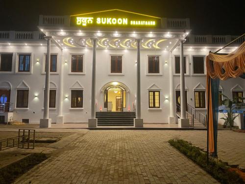 Hotel Sukoon Bharatgarh في Rūpnagar: مبنى أبيض عليه علامة في الليل