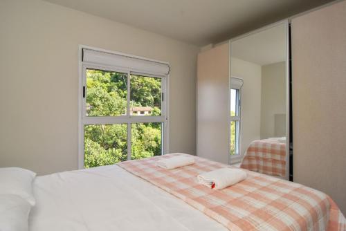 a white bedroom with a bed and a window at Apto 2 quartos, 350 mts Primavera Garden e ACM P2079 in Florianópolis