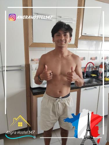 a shirtless man standing in a kitchen giving thumbs up at Angra Hostel 147 in Angra dos Reis