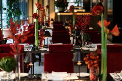 a dining room with tables with red chairs and flowers at Portrait Milano - Lungarno Collection in Milan