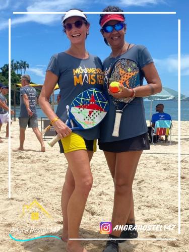 two women standing on the beach holding tennis rackets at Angra Hostel 147 in Angra dos Reis