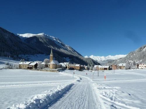 a snow covered road with a church in the distance at Biala - BioBergün in Bergün