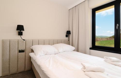 a bedroom with a bed with white sheets and a window at Skalnica - Apartamenty w Bieszczadach nad Soliną in Berezka
