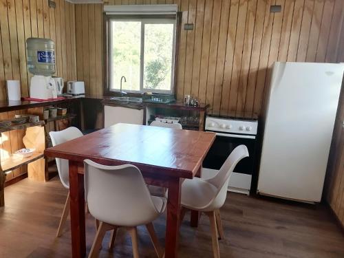eine Küche mit einem Holztisch und weißen Stühlen in der Unterkunft Cabaña CyG 2 - Chaitén in Chaitén