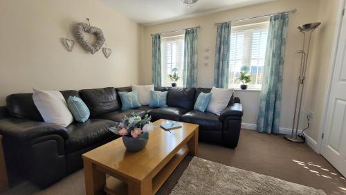 a living room with a black leather couch and a coffee table at Puddleduck Cottage - Part of the The Bay Filey Holiday Village with pool, gym and direct beach access, pub, restaurant, tennis and meadows walks in Filey