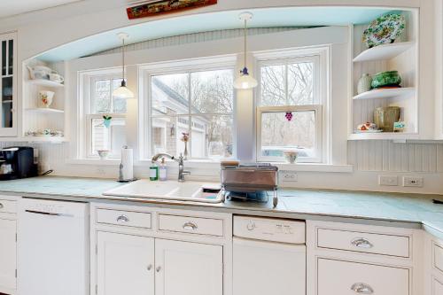 uma cozinha com armários brancos, um lavatório e duas janelas em Lovely on Llewellyn em Edgartown