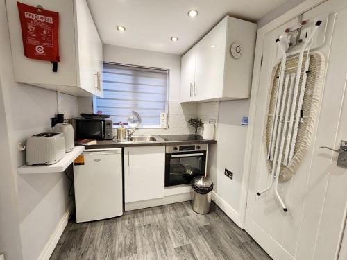 een kleine keuken met witte kasten en een wastafel bij Studio Apartment The Den Colnbrook in Colnbrook