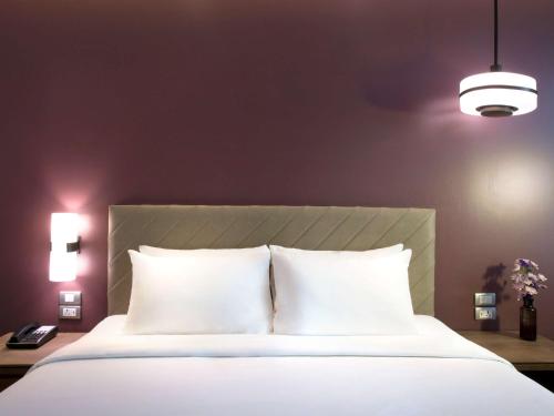 a bedroom with a white bed with two pillows at Mercure Bangkok Sukhumvit 24 in Bangkok