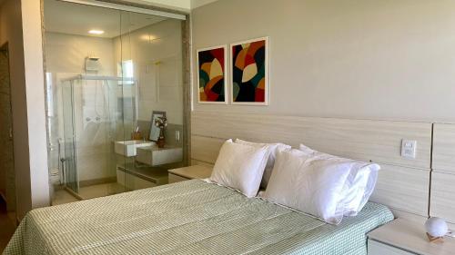 ein Schlafzimmer mit einem Bett mit weißen Kissen und einem Badezimmer in der Unterkunft Kalug - Duplex PÉ NA AREIA com 4 suítes, piscina e churrasqueira privativa na Praia do Sul! Perfeito para família - Wifi 300mb! in Ilhéus