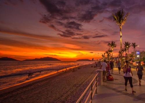 a group of people walking on the beach at sunset at LOFT PLAYAS "A" , a unos pasos del malecon estadio acuario y letras in Mazatlán